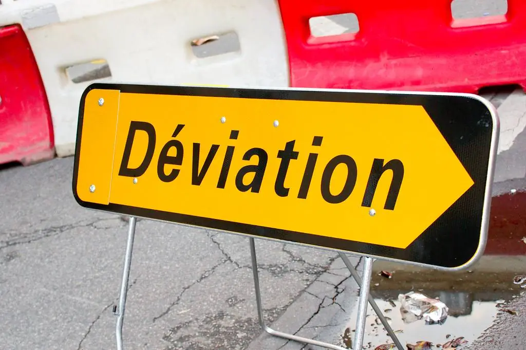 Un panneau jaune « Déviation » posé sur un trottoir, devant des barrières de chantier.