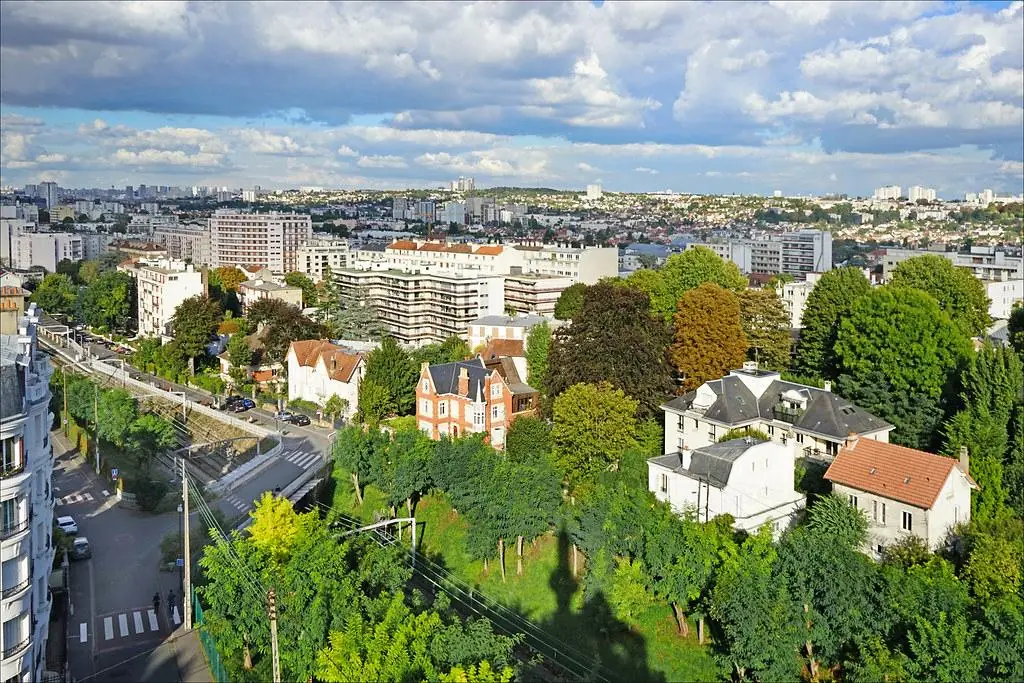Une ville vue d'en haut : toits, immeubles et jardins jusqu'à l'horizon.